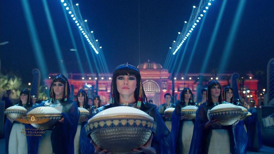 Pharaoh-Core: How GEM’s Opening Is Reigniting Ancient Egypt Style 1 1 Performers in the Pharaohs’ Golden Parade wearing Cleopatra-style wigs and blue costumes, carrying large decorated vessels in a night-time procession outside the Egyptian Museum in Cairo