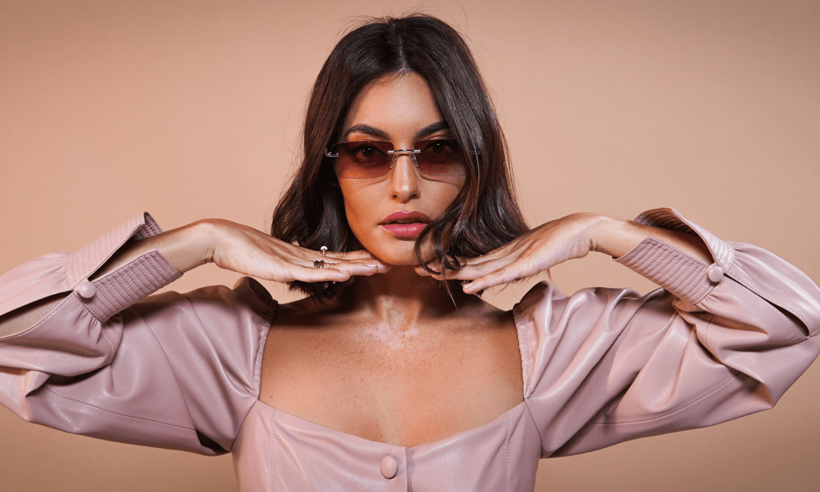 Karen Wazen in Egypt: How Her Eyewear Became a Regional Power Move Suggested slug 1 1 Woman in a blush pink faux-leather top and tinted narrow sunglasses, posing with both hands framed under her chin against a nude background