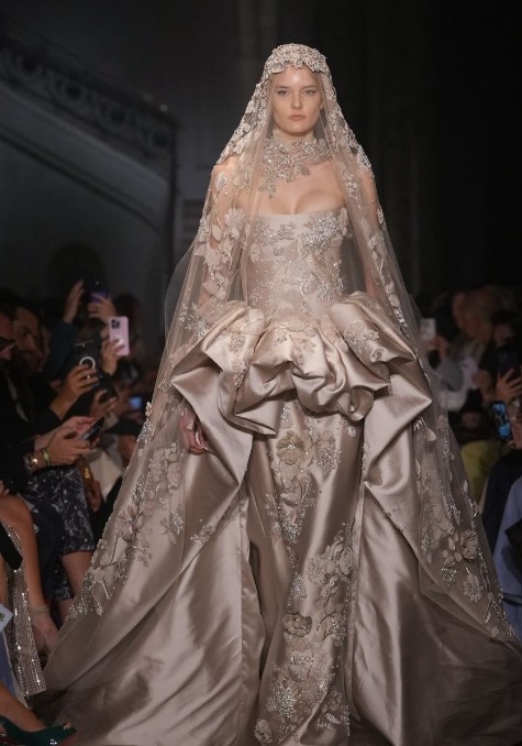 Runway model in champagne-gold couture bridal gown with dramatic sculpted skirt and embellished veil at a Middle East fashion show