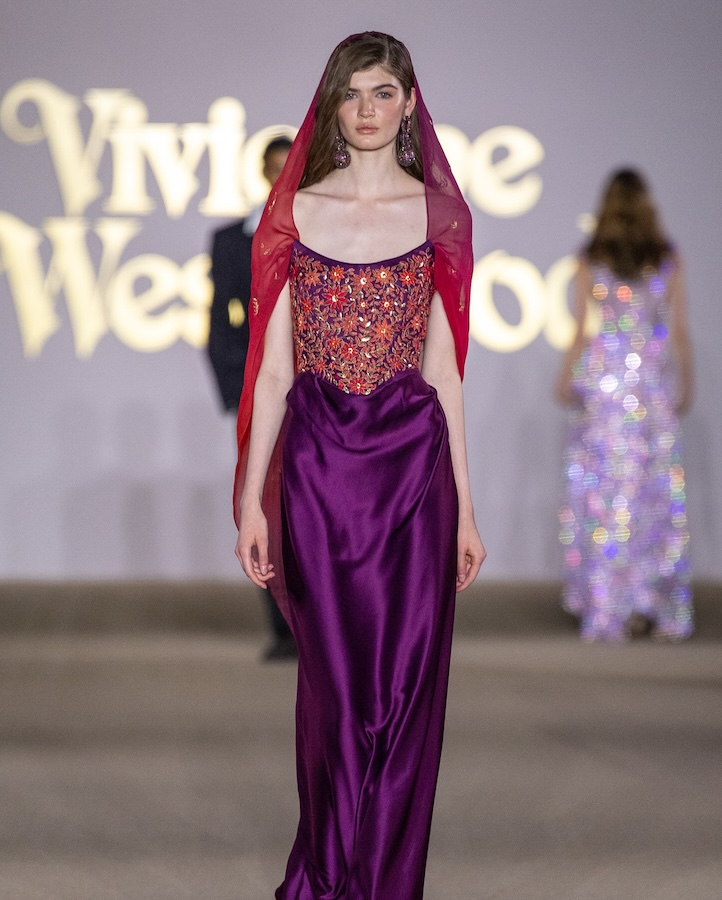 Riyadh Fashion Week 2025: From Local Talent to Vivienne Westwood’s Middle East Debut 1 1 Model walking the Vivienne Westwood runway in a purple satin gown with an embroidered red and orange bodice, styled with a sheer red veil over her hair.
