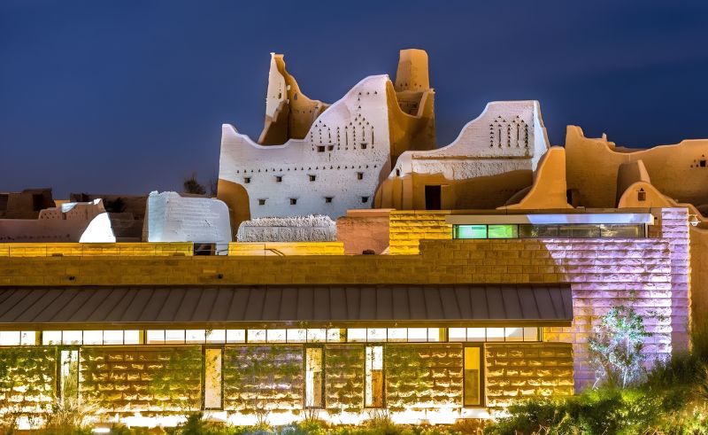 Night view of traditional mud-brick architecture overlooking a modern building illuminated at Al Diriyah.