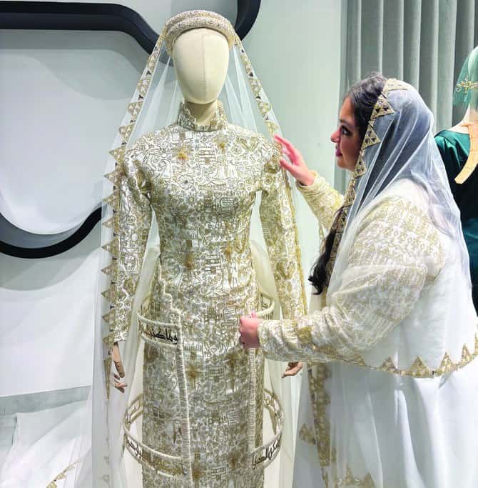 Designer adjusting a gold-embroidered traditional dress on a mannequin, highlighting intricate craftsmanship and detailing.
