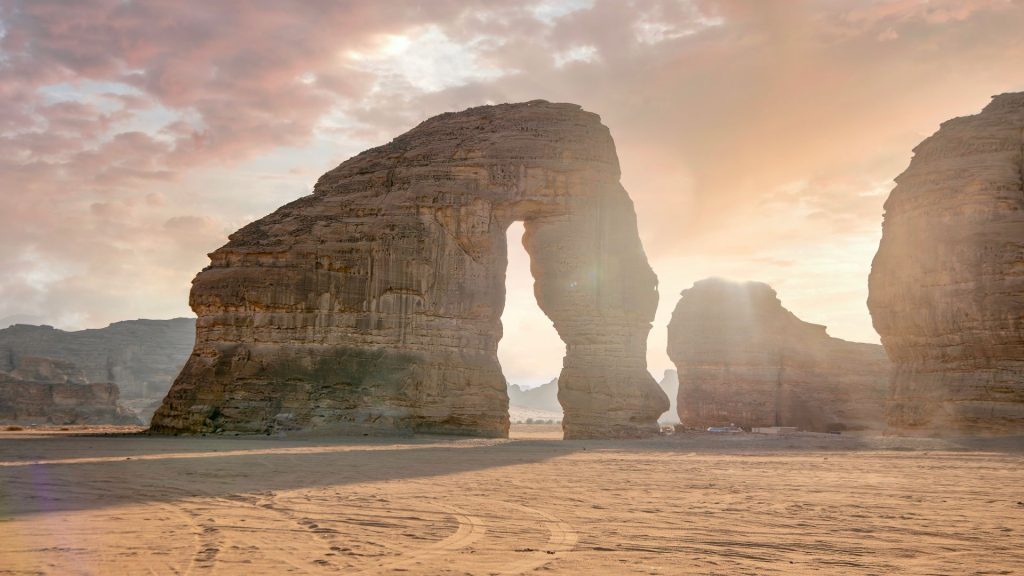 Sandstone rock formation with a natural arch in AlUla’s desert landscape at sunset.