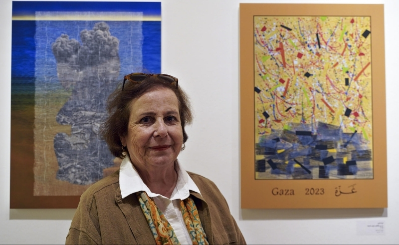 Artist standing beside abstract paintings referencing Gaza 2023, displayed as part of a contemporary art exhibition highlighting regional narratives and personal expression.