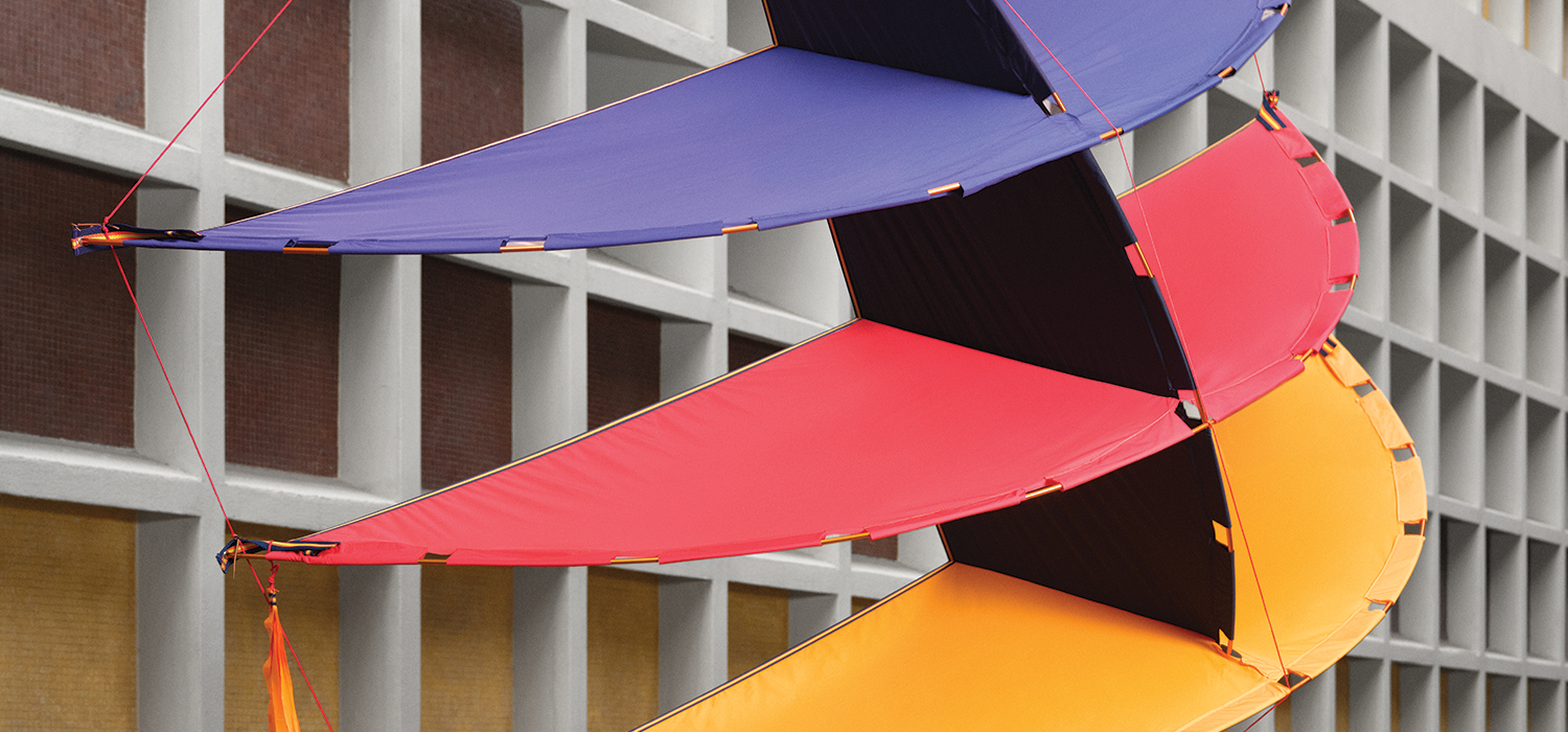 Colorful textile installation suspended across a Milan architectural façade, reflecting Salone in the City’s dialogue between design, urban space, and temporary artistic intervention.
